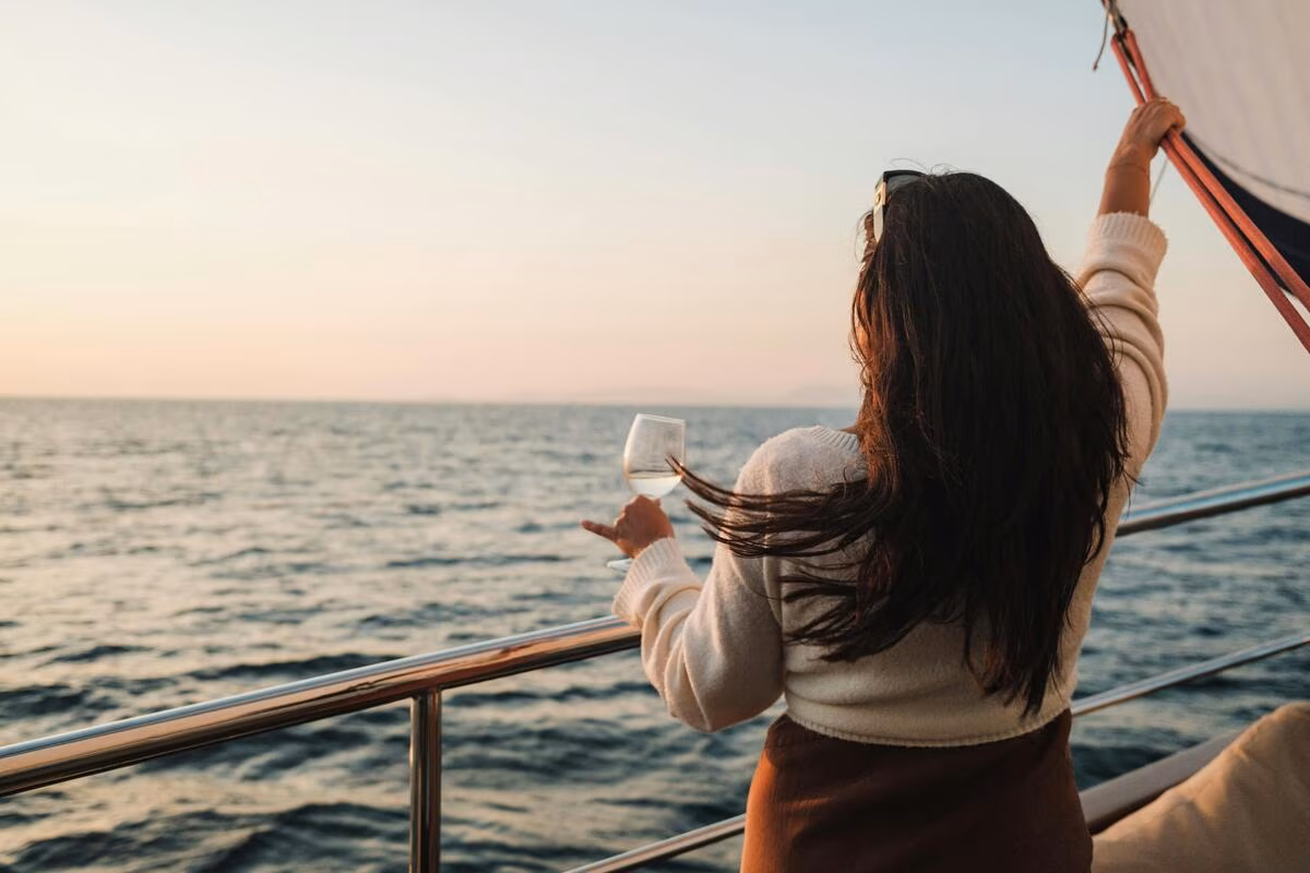 Woman with long hair holding a wine glass, enjoying a sunset sailing on a boat.