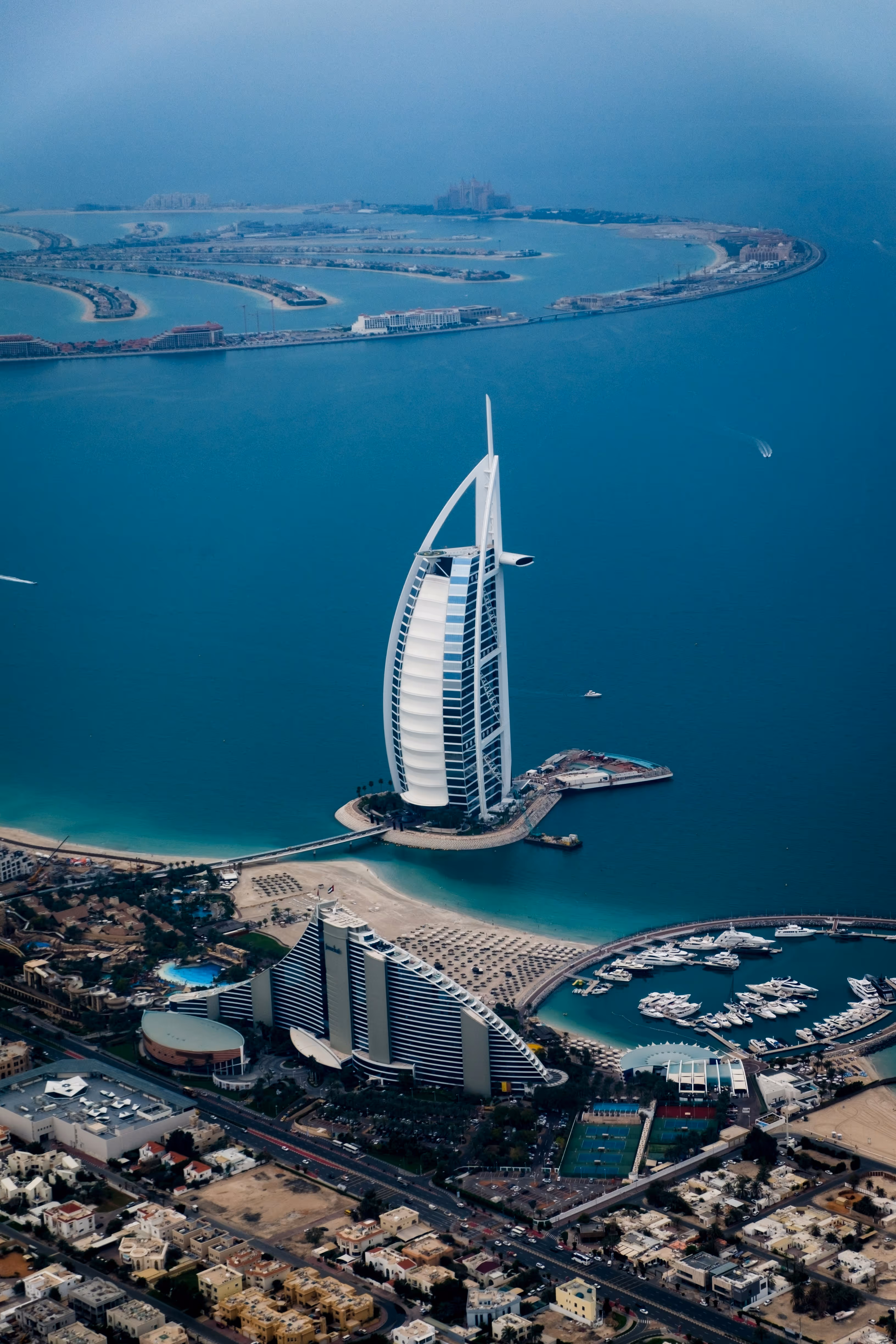 Aerial view of Burj Al Arab hotel surrounded by blue waters and nearby marina in Dubai.