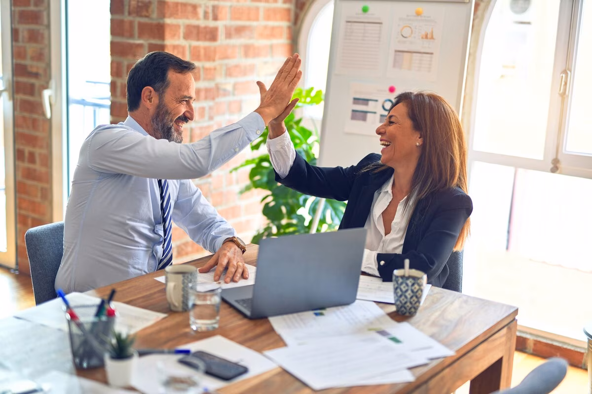 Businessman and businesswoman smiling and giving a high five in a modern office setting.