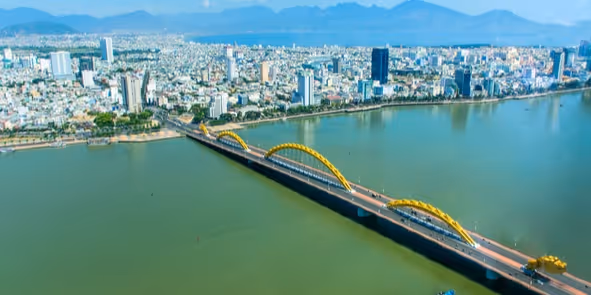 Aerial view of a city with a river and a long bridge featuring distinctive yellow arches.