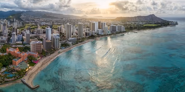 Aerial view of Honolulu with a beach, high-rise buildings, and Diamond Head crater in the background at sunset.