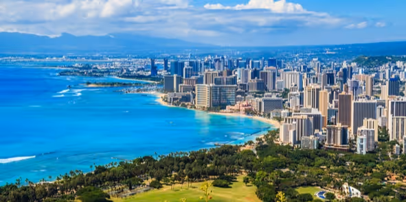 Aerial view of a coastal city with high-rise buildings, a blue ocean, and green parkland in the foreground.