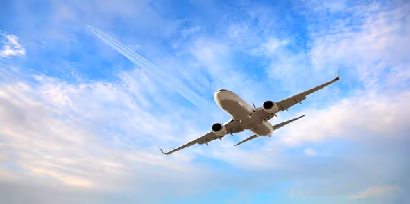 Commercial airplane flying upward against a partly cloudy blue sky with a contrail behind.