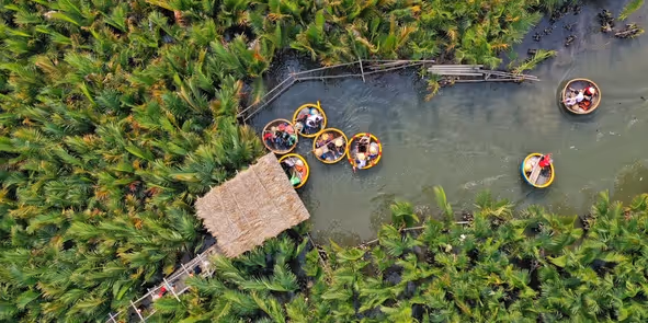 Aerial view of people riding traditional round bamboo basket boats on a narrow waterway surrounded by dense green vegetation.
