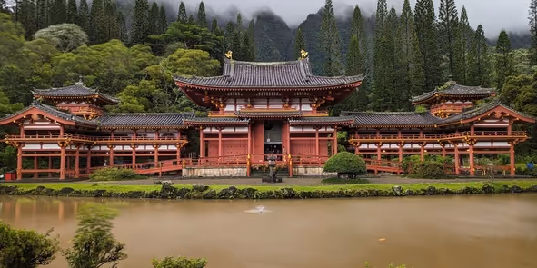 Traditional red Japanese temple surrounded by green trees and reflected in a calm pond.