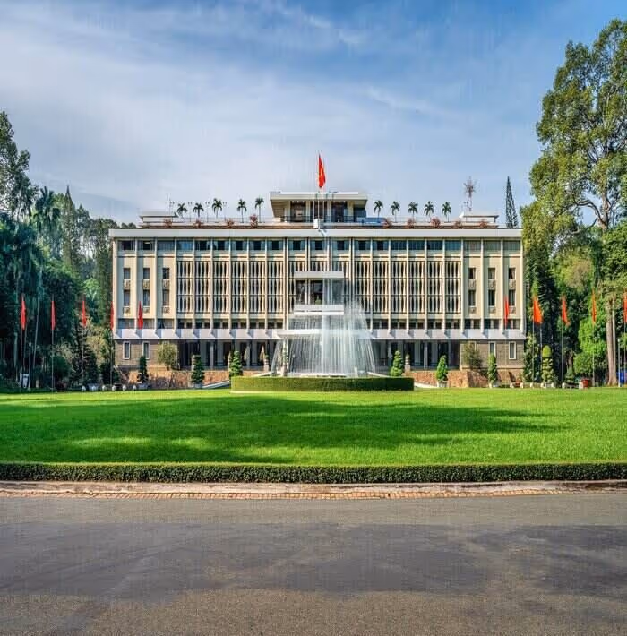 Large government building with multiple floors, a central water fountain, and green lawn in front under a partly cloudy sky.